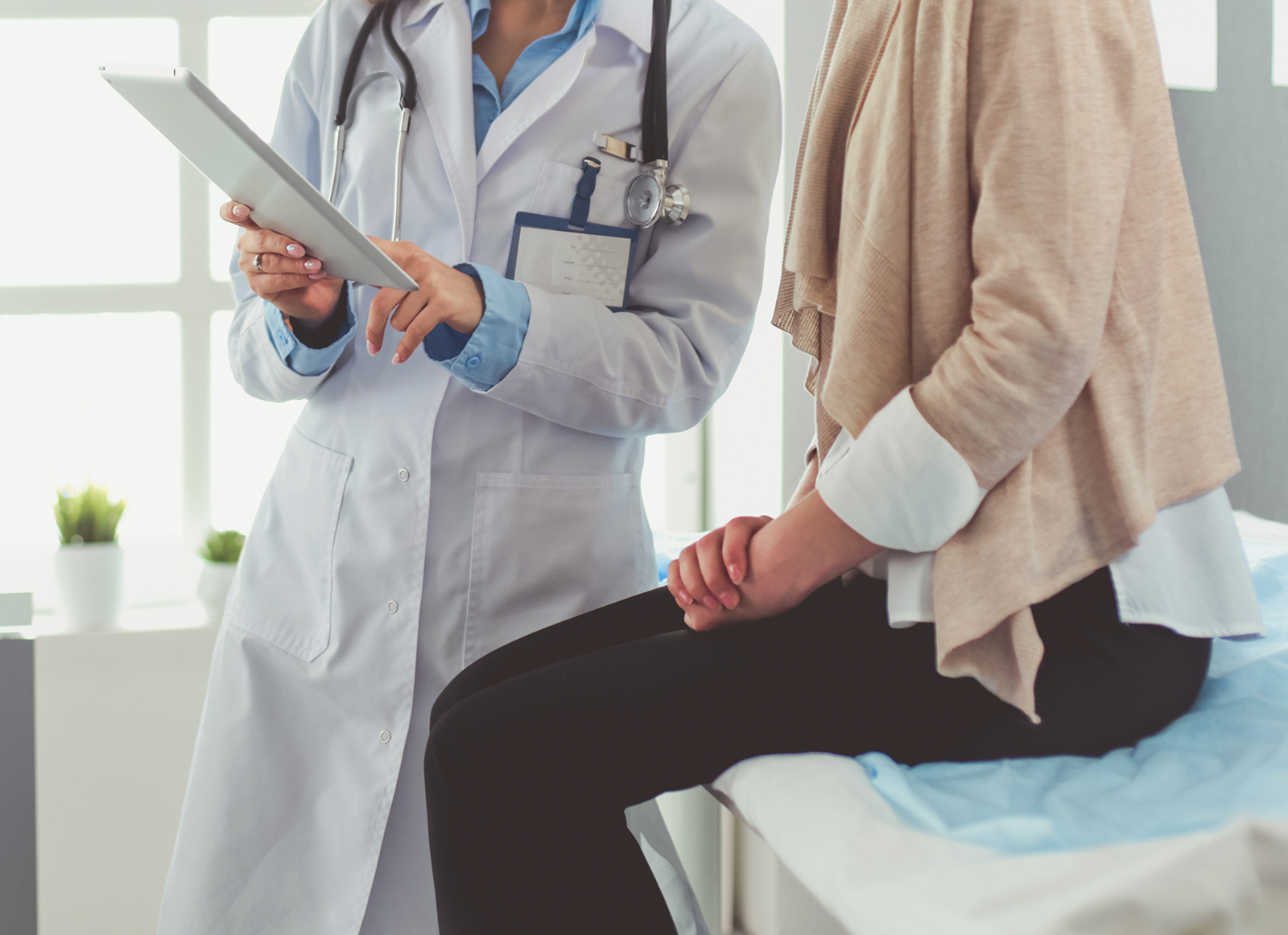 doctor pointing to clipboard while talking to female patient in exam room sitting on table